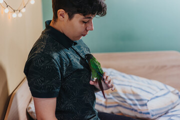 A young person sits in a cozy bedroom, gently interacting with a colorful parrot. The warm interior...