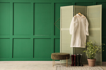 Interior of hallway with raincoat on folding screen, pouf and gumboots