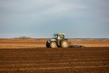 Tractor with a plow attachment tilling the soil in a vast farmland setting