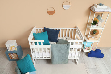 Stylish crib with plaid and shelving unit near beige wall in interior of children's room