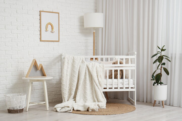 Beautiful crib with plaid and lamp near white brick wall in interior of children's room