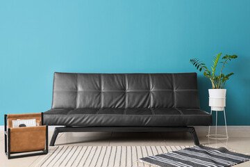 Black leather sofa, houseplant and magazine holder in living room