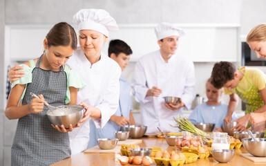 Adult woman cook helps little girl cook at cooking master class