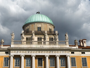 Trieste, Italy - June 26, 2024: Palazzo Carciotti upper level with its row of classical statues and its golden dome under gray cloudscape