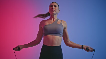 Fit girl jumping rope in neon studio background. Woman making jump exercise