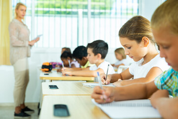 Group of focused pupils sitting at classroom working at class with teacher