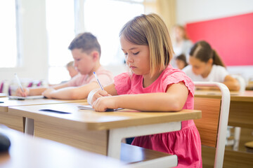 Portrait of cute intelligent schoolgirl who writing exercises at lesson in primary school