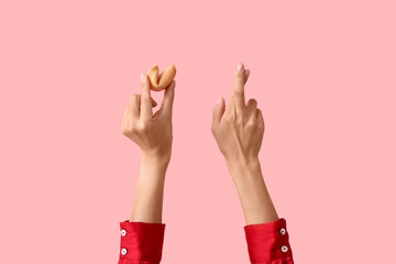 Female hands with fortune cookie and crossed fingers on pink background, closeup