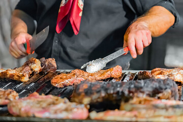 Chef wearing red bandana, grilling steaks over open flame on barbecue, carefully cooking meat to perfection