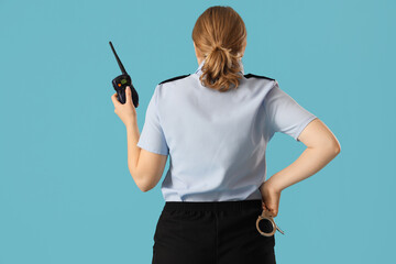 Young female police officer with radio transmitter and handcuffs on blue background, back view....