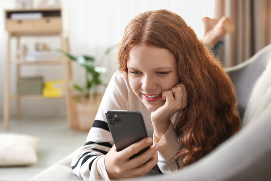 Beautiful teenage girl using smartphone on sofa at home