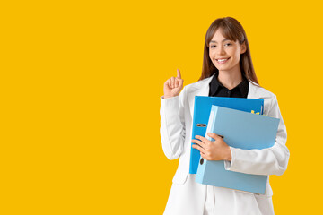 Fototapeta premium Beautiful businesswoman with folders pointing at something on yellow background