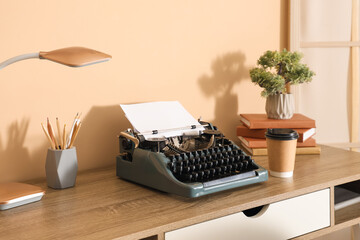 Vintage typewriter and cup of coffee on table near beige wall