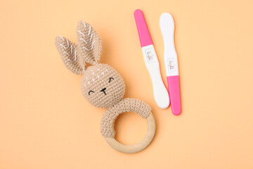 Pregnancy tests and baby rattle on pale orange background, top view