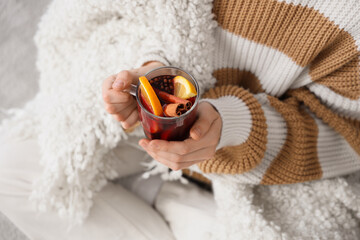 Young woman in warm sweater with glass cup of hot mulled wine at home, closeup