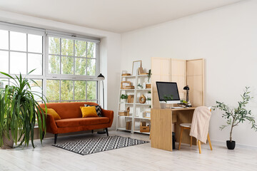 Interior of stylish living room with brown sofa, folding screen and comfortable workplace