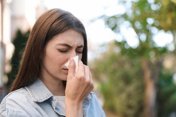 Woman with runny nose in park, space for text