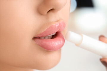 Naklejka premium Beautiful young woman applying lip balm in bathroom, closeup