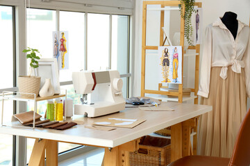 Tailor's workplace with sewing machine and patterns near window in atelier
