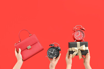 Female hands with bag, alarm clocks and gift on red background. Black Friday Sale