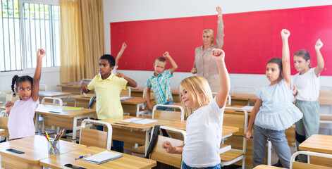 Portrait of preteen schoolchildren with female teacher performing daily physical exercises in...