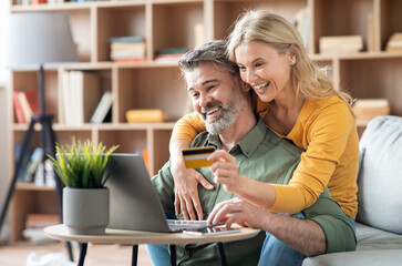 Beautiful Middle Aged Couple Making Order From Internet With Laptop And Credit Card, Happy Mature Spouses Doing Online Shopping Or Virtual Payments While Relaxing With Computer At Home, Free Space