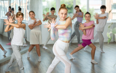 Naklejka premium Teenagers in classroom dance and learn modern dances, participants of lesson move in staggered manner to beat of energetic music. Female teacher in background dances with students