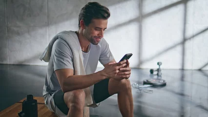 Gordijnen Smiling sportsman looking mobile phone after training closeup. Guy messaging © stockbusters