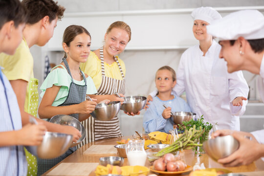Positive interested teenage girl participating group culinary class for kids, engrossed in cooking process and talking friendly to other participants