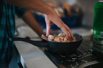 A close-up image of a person preparing chicken pieces in a skillet on the stove top, emphasizing home cooking and culinary skills.