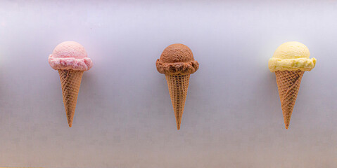 A row of strawberry, chocolate and vanila ice cream cones on a white background
