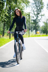 Fototapeta premium Caucasian woman riding a bike in a park. Vertical photo. 