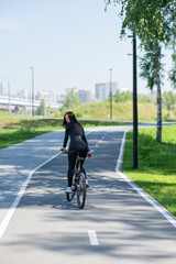 Rear view of Caucasian woman riding bike in park. Vertical photo. 