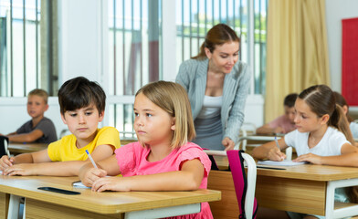 Fototapeta premium Portrait of small school girl and boy sitting together in classroom during lesson in elementary school
