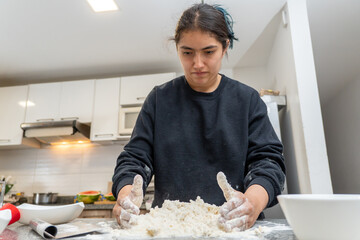 Young woman with black hair tied up uses flour for baking