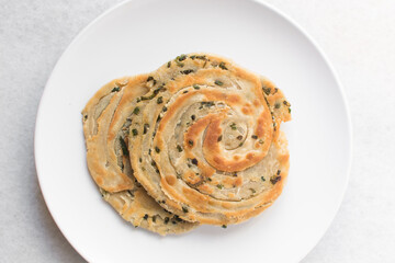 Overhead view of chinese scallion pancakes on a white plate, top view of golden-brown homemade scallion pancakes, process of making cong you bing