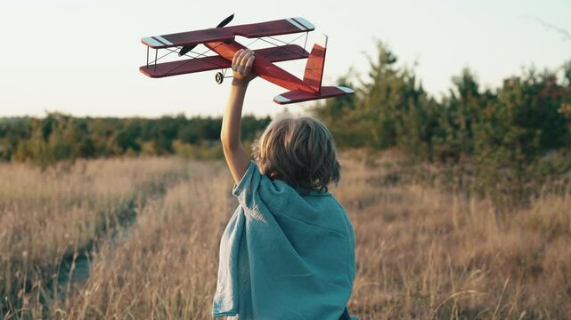Unrecognizable 5 years old child boy running with wooden vintage airplane. Kid dreaming to be pilot. Imagination freedom, travel everywhere, active childhood