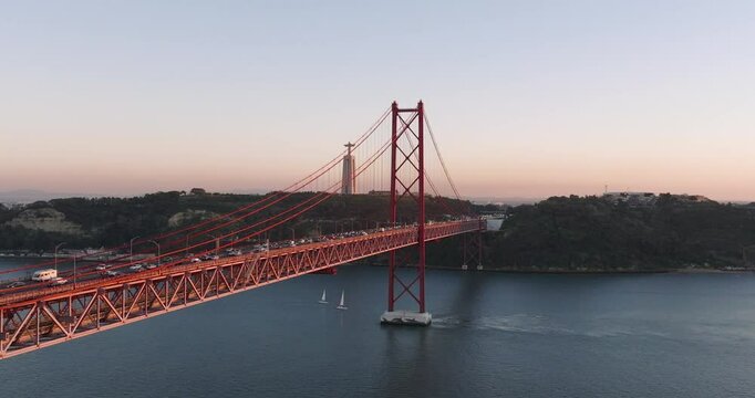 Aerial drone shot towards the 25th April Bridge, Ponte 25 de Abril, and Cristo Rei in Lisbon, Portugal, Europe. Golden hour before sunset at end of autumn, start of winter. Shot in ProRes 422 HQ
