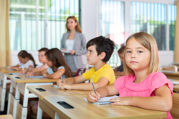 Fototapeta na wymiar Portrait of tired schoolgirl sitting in classroom during lesson in elementary school