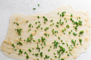 Overhead view of green scallions on oiled pancake dough, top view of sliced green onion on rolled out scallion pancake dough, process of making flaky scallion pancake