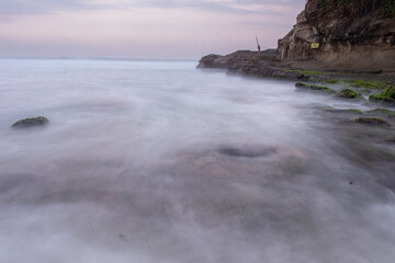 the beautiful view of a tropical beach in the morning, with white sand and coral rocks hit by ocean waves. Landscape images are taken with slow speed technique.