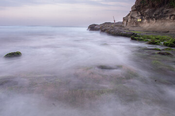 the beautiful view of a tropical beach in the morning, with white sand and coral rocks hit by ocean waves. Landscape images are taken with slow speed technique.