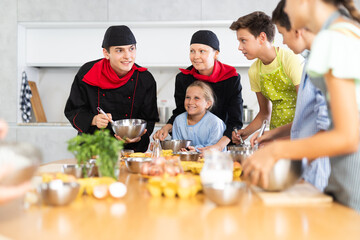 ..Young guy and adult woman chef at master class teaches group of children how to cook food
