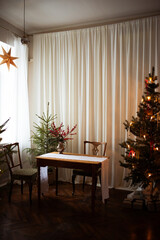 Long beige white candles in a candlestick with brown velvet bows. Christmas trees and fir tree branches on a brown wooden table