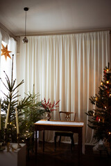 Long beige white candles in a candlestick with brown velvet bows. Christmas trees and fir tree branches on a brown wooden table