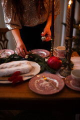 Close up of a woman hand serves festive laying table, preparation for christmas dinner, preparation for christmas dinner. Christmas tree, fir tree branches, pomegranate and traditional Christmas stol