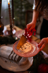 Closeup of unrecognizable woman cuts and serves a stollen ant sets up dining table for Christmas decorated with fir branches and candles in grey tones, copy space