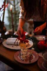 A girl is setting a beautifully arranged dining table with candles, festive decorations, and greenery, creating a warm atmosphere for a holiday celebration.