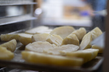 Steam coming out of hot peeled potatoes sitting on a rack in a restaurant kitchen.