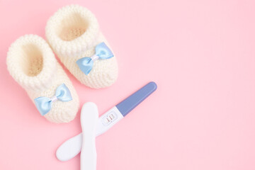 Pregnancy tests and knitted booties on pink background, top view. Space for text